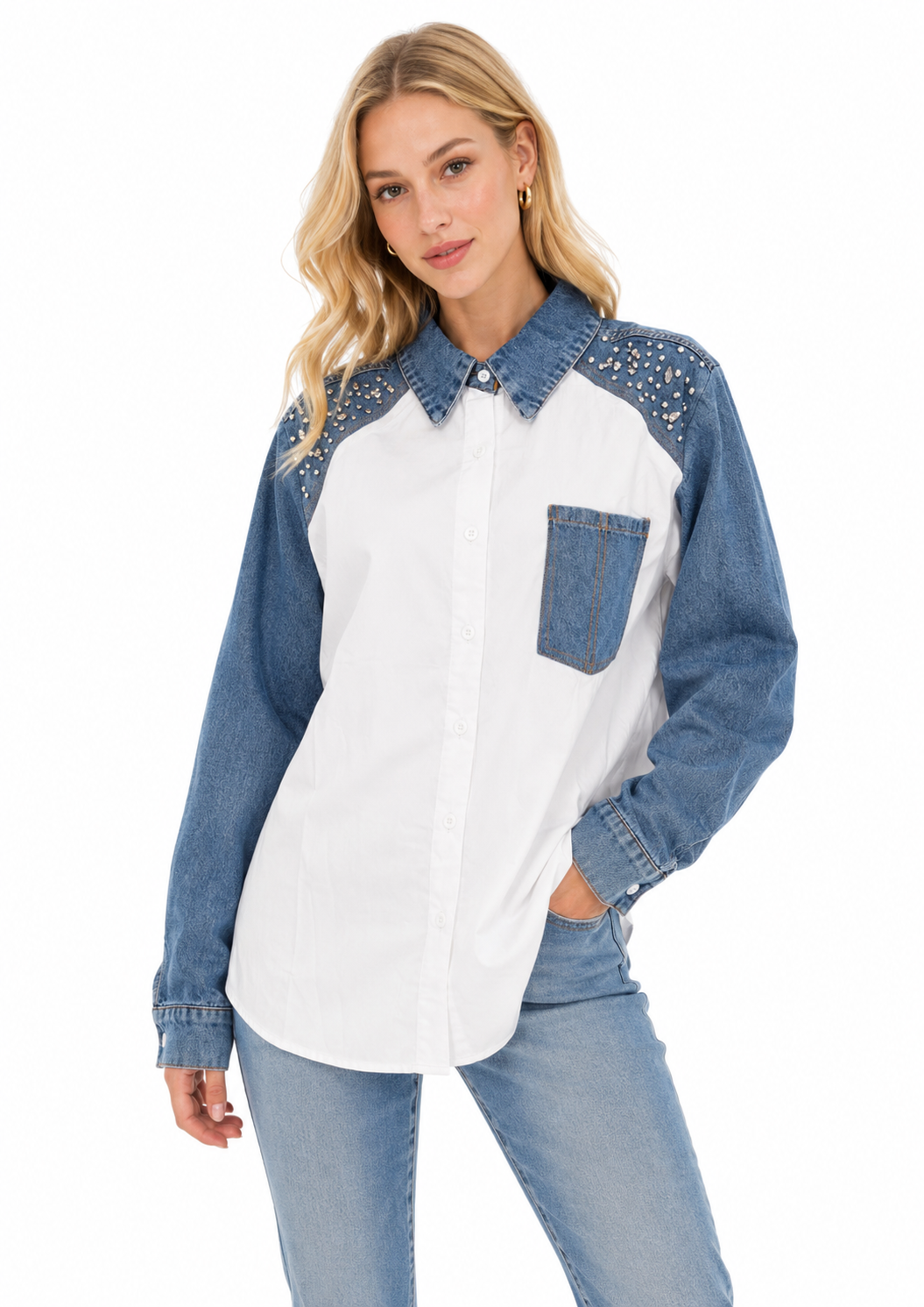 A woman modeling a long-sleeve western-style shirt with a white body, blue denim sleeves and collar, and silver rhinestone embellishments on the shoulders, paired with blue jeans against a white background.